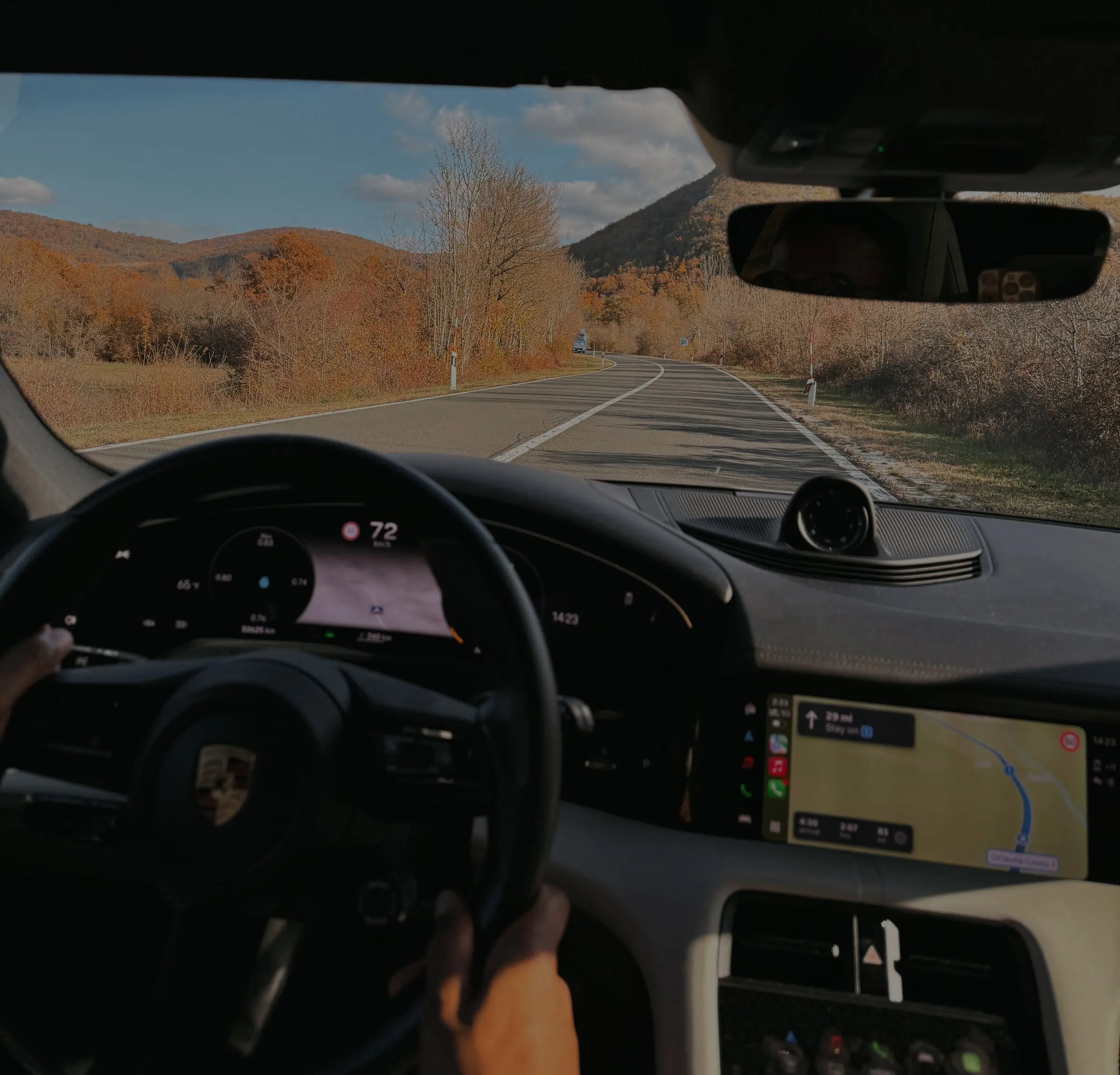 Driving a Porsche Taycan on an open road through autumn hills