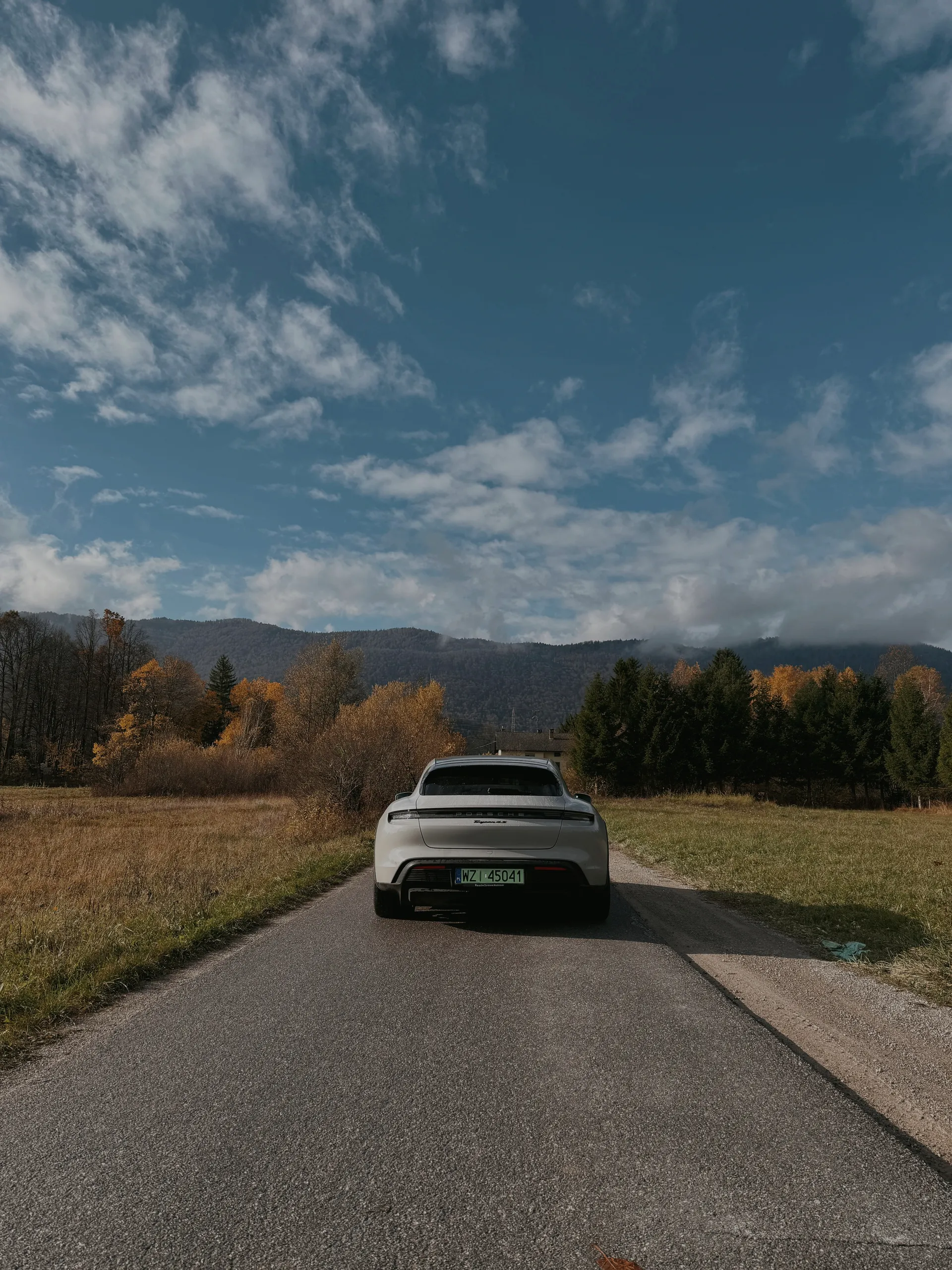 Porsche Taycan driving away down a rural mountain road in autumn